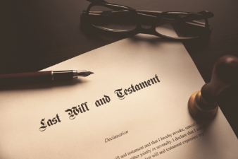 Last Will and Testament with a pen, eyeglasses and stamp resting on it